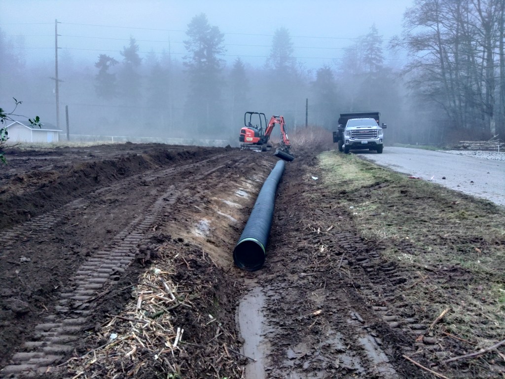 An illustration of a man operating an excavator, cutting a trench in his yard in front of a suburban home.